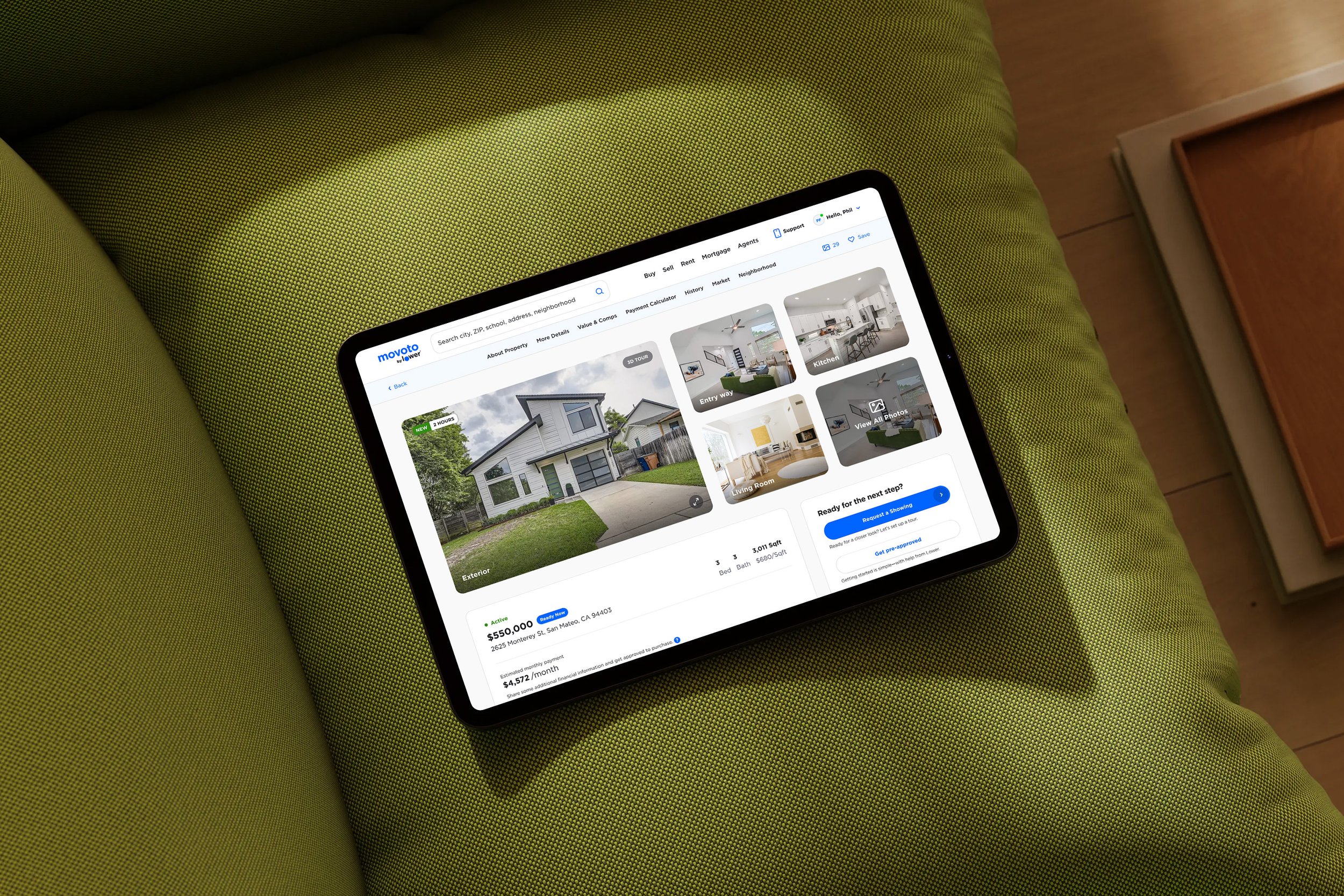 iPad showing a real estate listing for a modern white house, placed on a green upholstered surface.