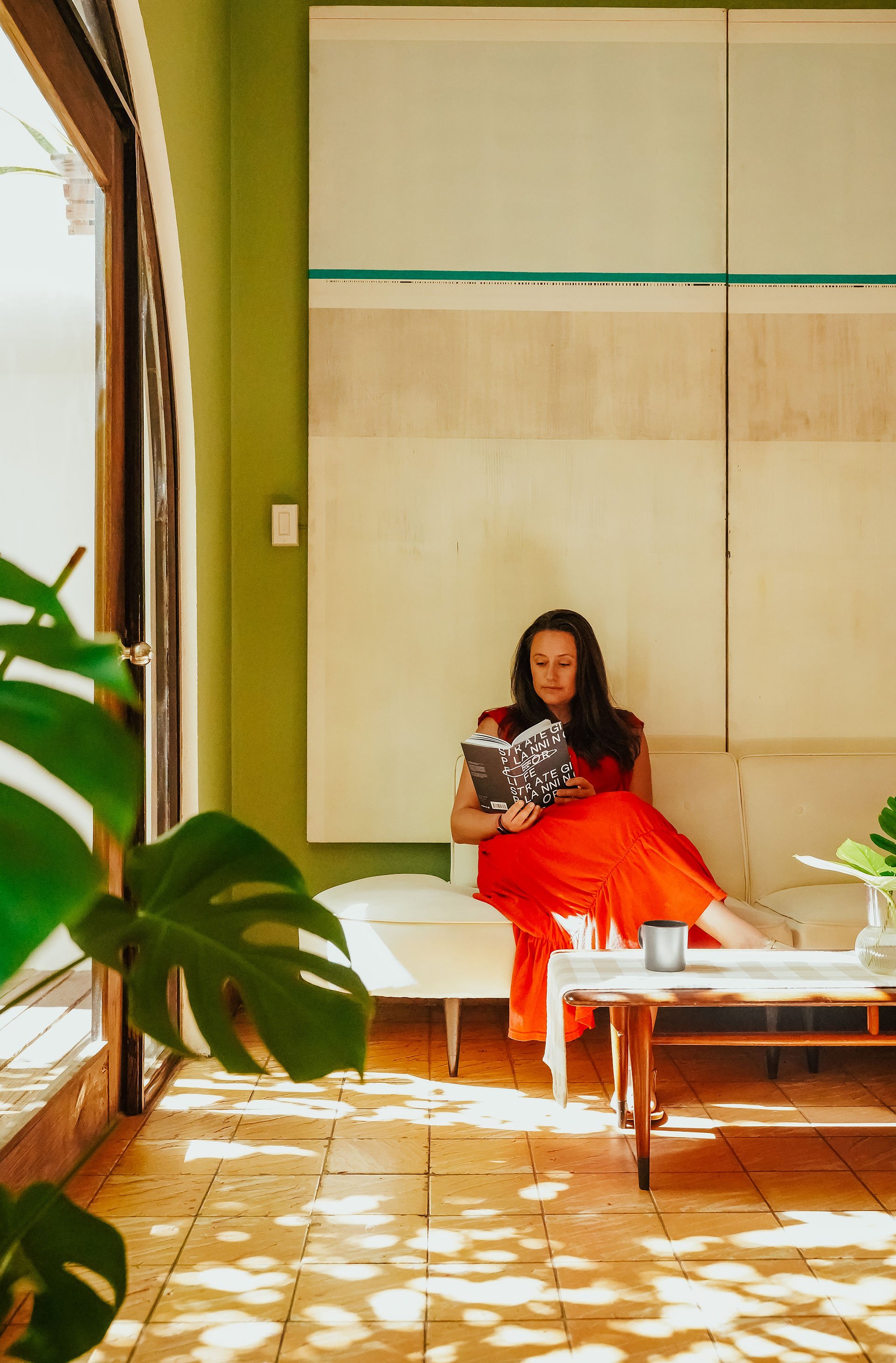 Woman in a red dress reading an Owl & Key guide on a white sofa.
