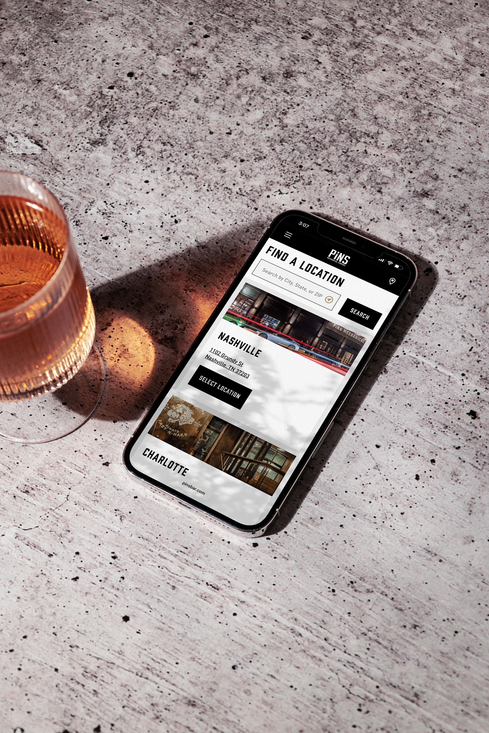 Phone on a table showing Pins locations for Nashville and Charlotte beside a drink.