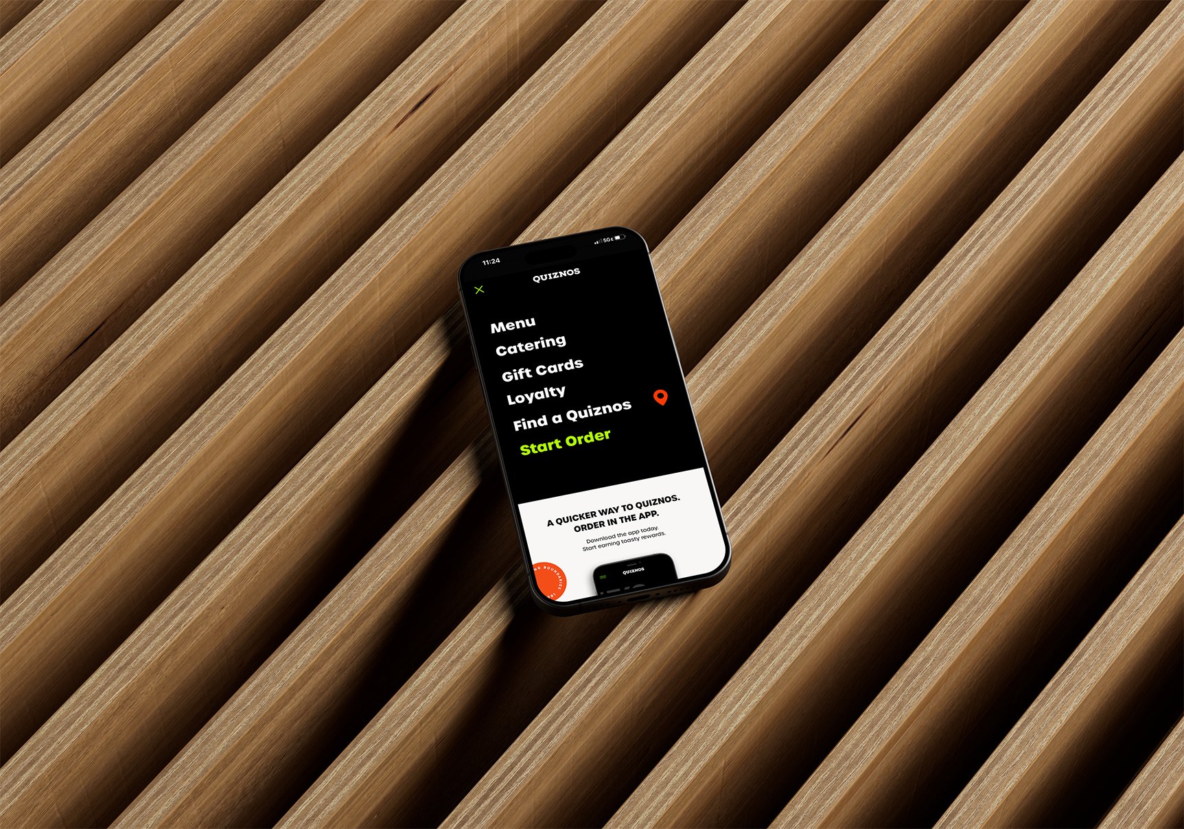 Smartphone on a wooden surface showing the Quiznos app menu.