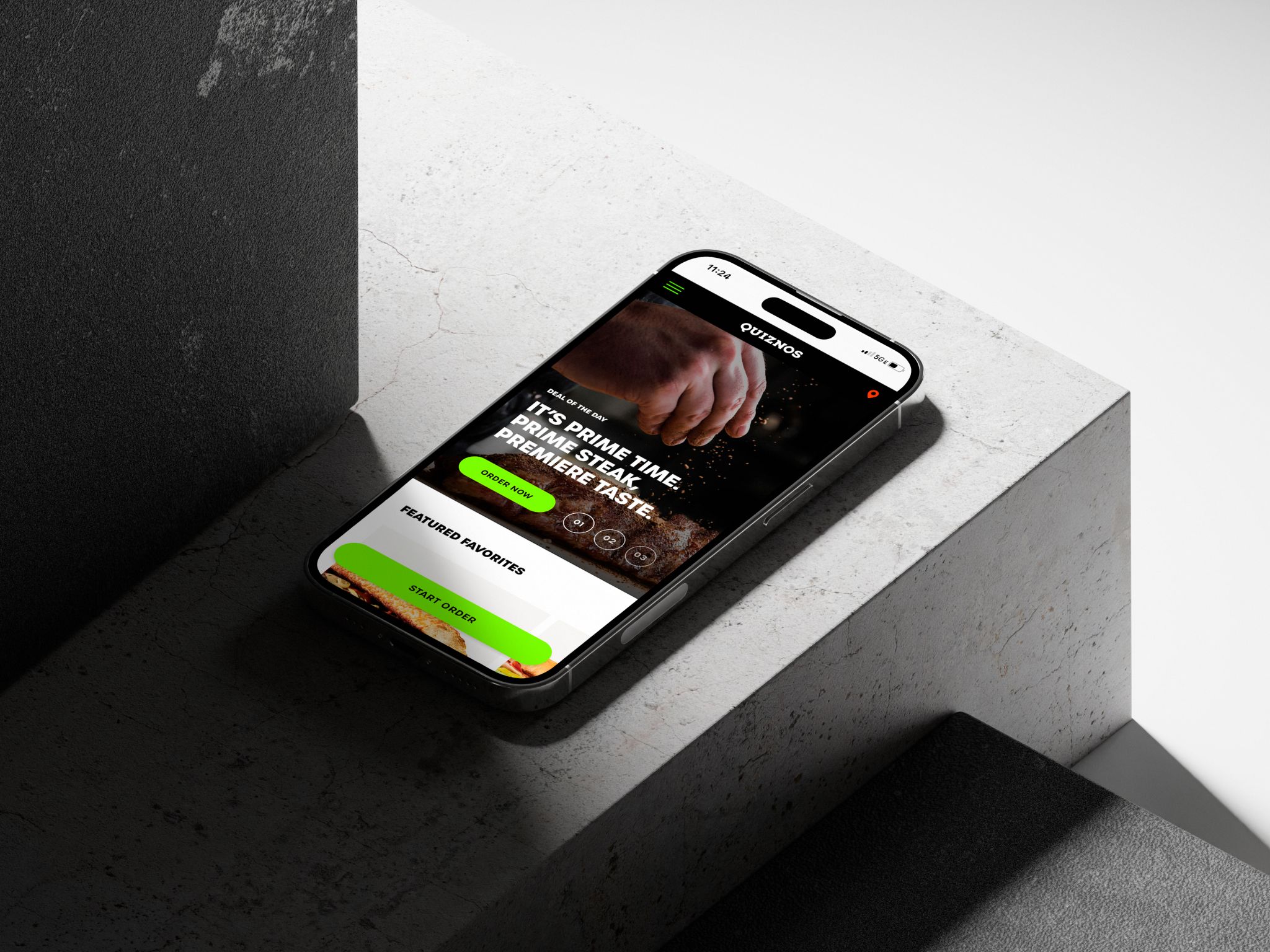 iPhone on a stone ledge showing the Quiznos app with Prime steak and Featured Favorites.