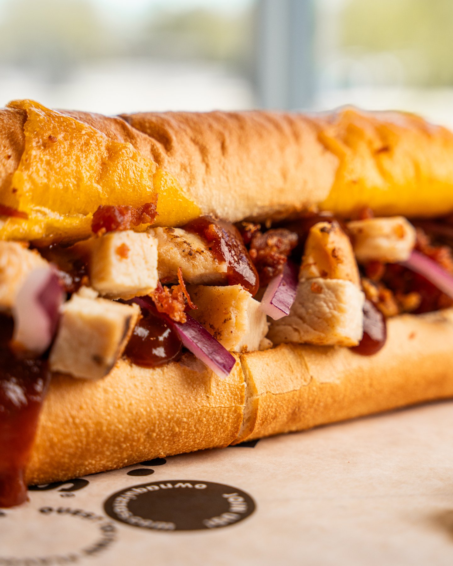 Close-up of a toasted Quiznos sandwich with chicken, cheese, bacon, and barbecue sauce.