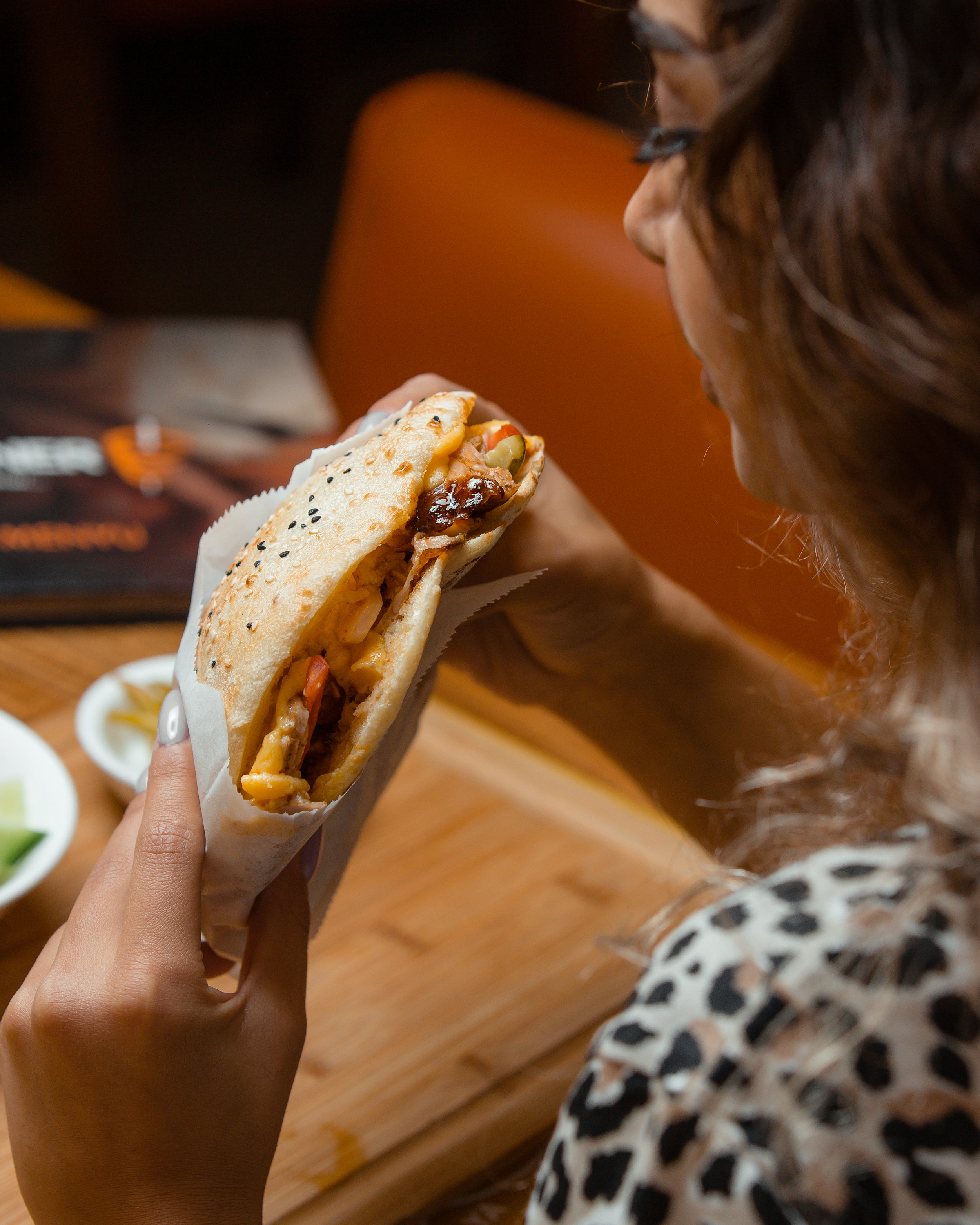 Person holding a wrapped Quiznos sandwich about to take a bite.