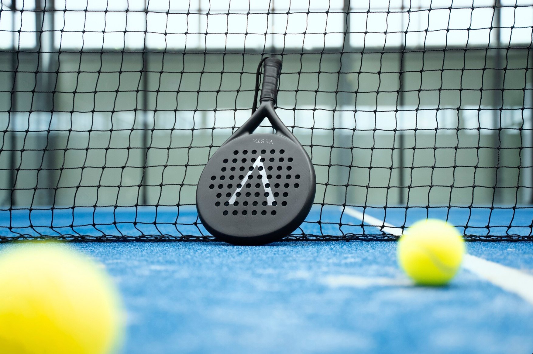 Racket leaning on a net on a blue court with two yellow balls.