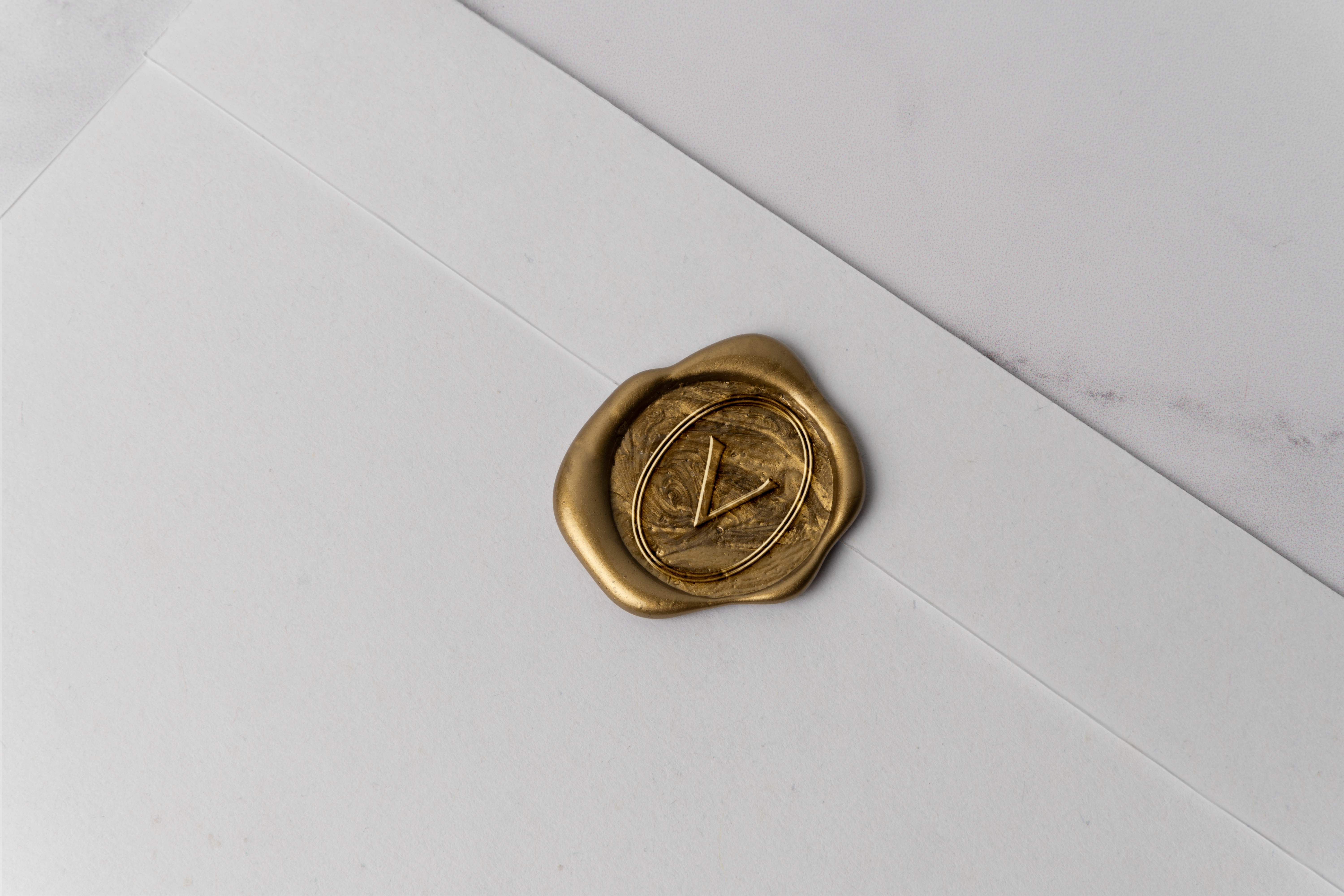Gold wax seal with a V mark on a white envelope.