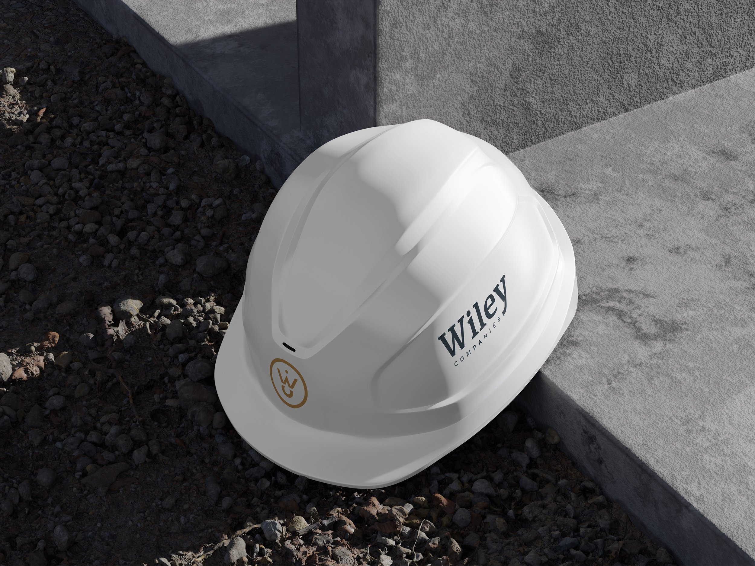 White Wiley Companies hard hat resting on rocky ground beside a concrete step.
